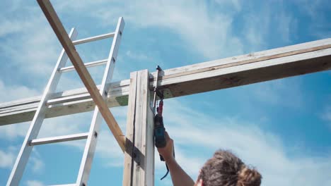 constructor en una escalera usando un destornillador eléctrico y una abrazadera para construir un marco de madera