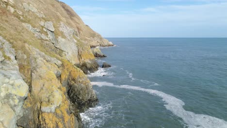 the perfect view of an edge of a cliff in this fly by shot that contains the tranquility of the soft blue skies and subtle waves of the sea