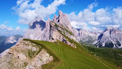 pull back aerial view from of the peaks of seceda with green pastures, and hiking trails in the foreground, and mountain peaks in the background in the italian dolomites in south tyrol, italy