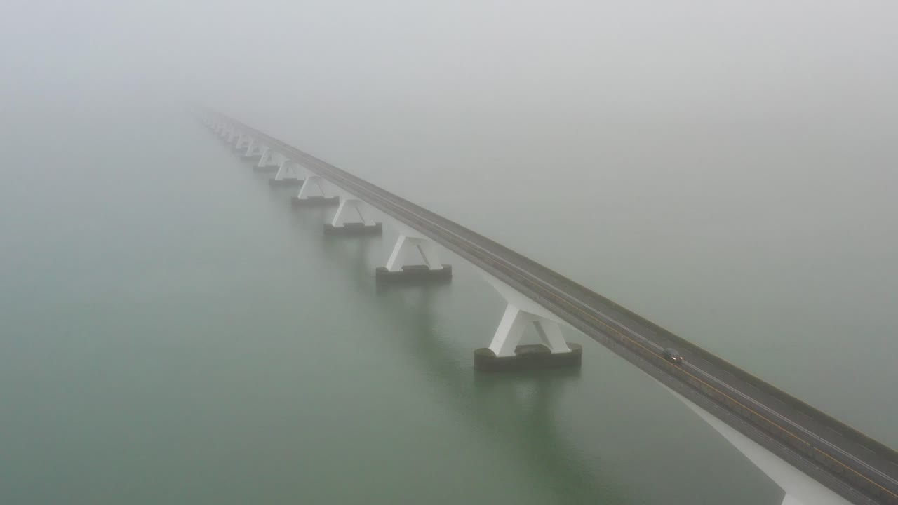 An almost empty bridge crossing the sea during thick fog, drone shot
