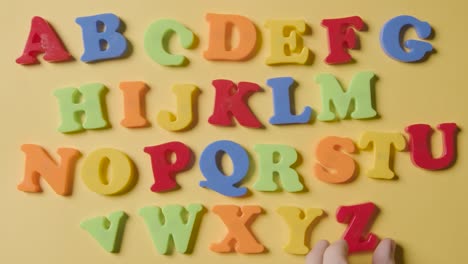 prise de vue en studio des lettres en plastique de l'alphabet disposées dans l'ordre sur un fond jaune 2