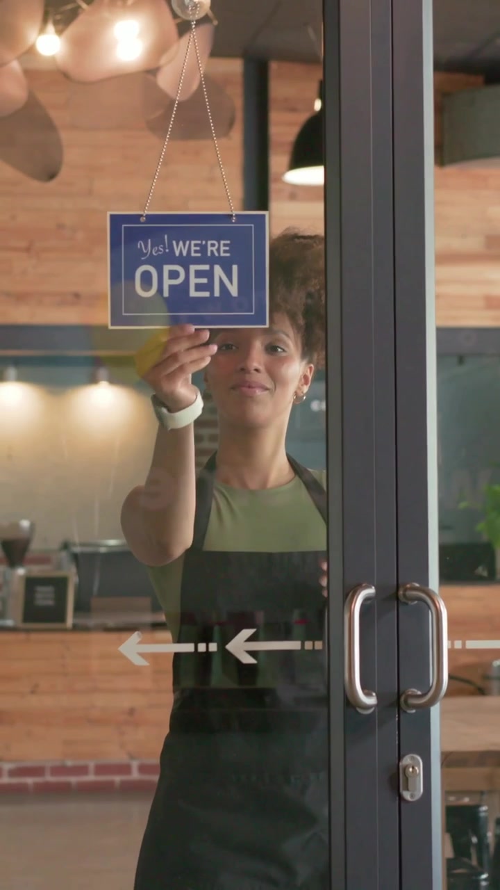 Vertical video: Walking barista in dark apron switching closed sign to open in cafe at opening