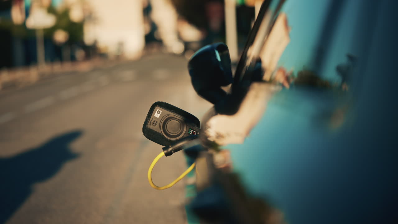 Electric car plugged into a charging port on the side of a city road, with evening traffic and headlights blurred in the background