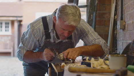 mature male carpenter in garage workshop planing piece of wood