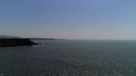 Imágenes-De-Drones-Moviéndose-A-Lo-Largo-Del-Mar-Abierto-Con-Montañas-En-La-Orilla-Mirando-El-Horizonte