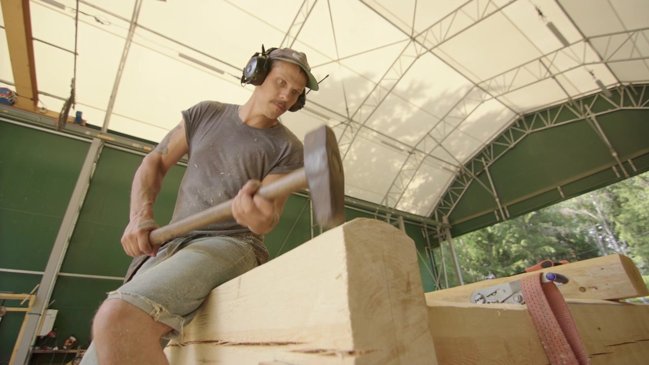 Carpintero con orejeras golpeando un tronco de madera para colocarlo con un mazo