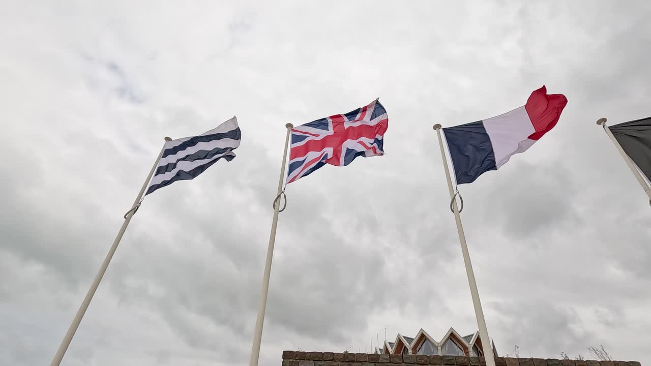 National flags wave on flagpoles at Dunkirk memorial, France, under overcast sky, daytime