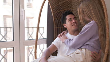 portrait of young couple looking out the window while sitting in a wicker chair together at home