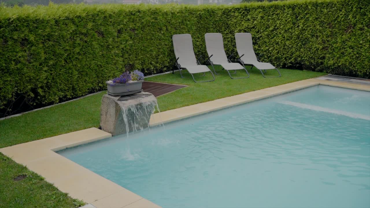 Outdoor swimming pool with three lounge chairs and a small water feature in a manicured garden