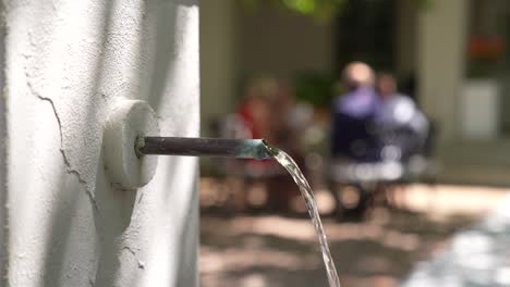 Close-Up-of-water-running-down-a-pipe,-with-people-sitting-at-the-back-blurred-out