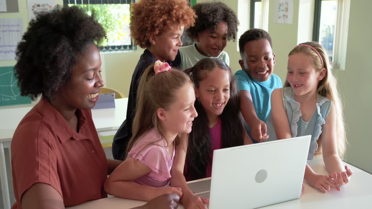 Studenti diversi, insegnante afroamericana in camicetta color ruggine che indica un portatile, che guarda e ride