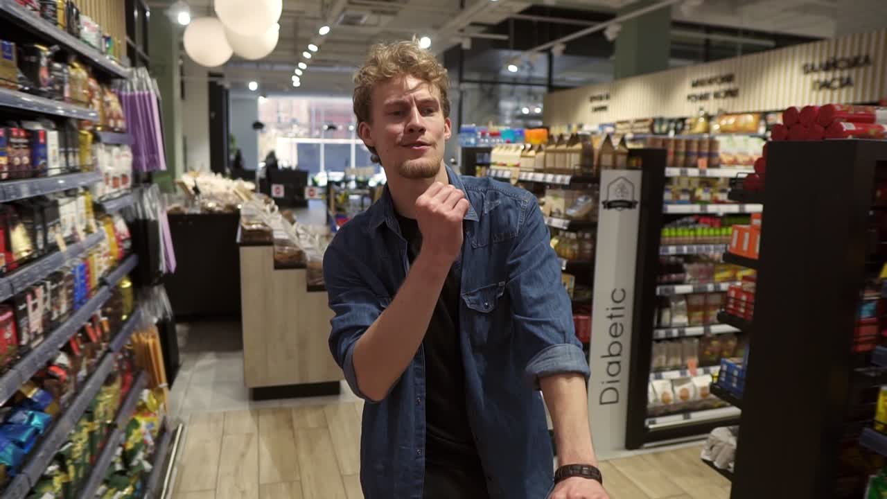 Excited young man in plaid shirt in supermarket dancing, funky moves close to shopping trolley. Positive dances in an empty food store row. Positive emotions. Slow motion
