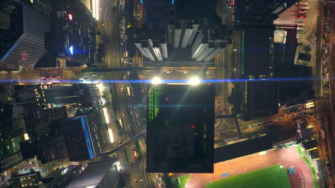 vuelo aéreo de arriba hacia abajo sobre una autopista concurrida y edificios de gran altura en wan chai, hong kong junto al estadio de atletismo por la noche