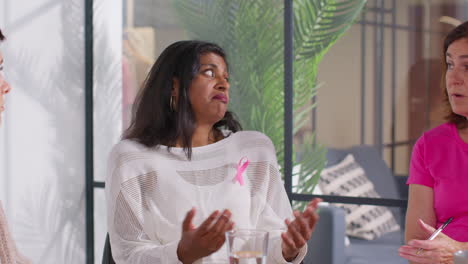 mature woman wearing pink breast cancer awareness ribbon talking at meeting of therapy support group for cancer treatment patients 4