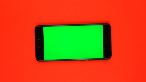 real smartphone with green screen rotates on red background.