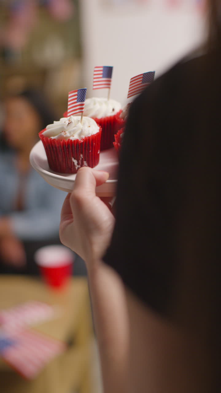 video vertical de una mujer en casa sirviendo pasteles con estrellas y rayas americanas en miniatura banderas a amigos en una fiesta que celebra el 4 de julio, día de la independencia