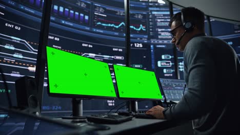 es un especialista profesional en soporte técnico y desarrollador de software que trabaja en una computadora con pantalla verde en una sala de control de monitoreo con pantallas digitales. el empleado usa auriculares.