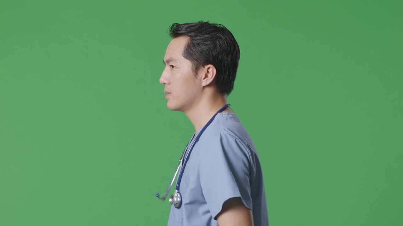 Primo piano di profilo di medico asiatico con stetoscopio che cammina su sfondo green screen in ospedale.