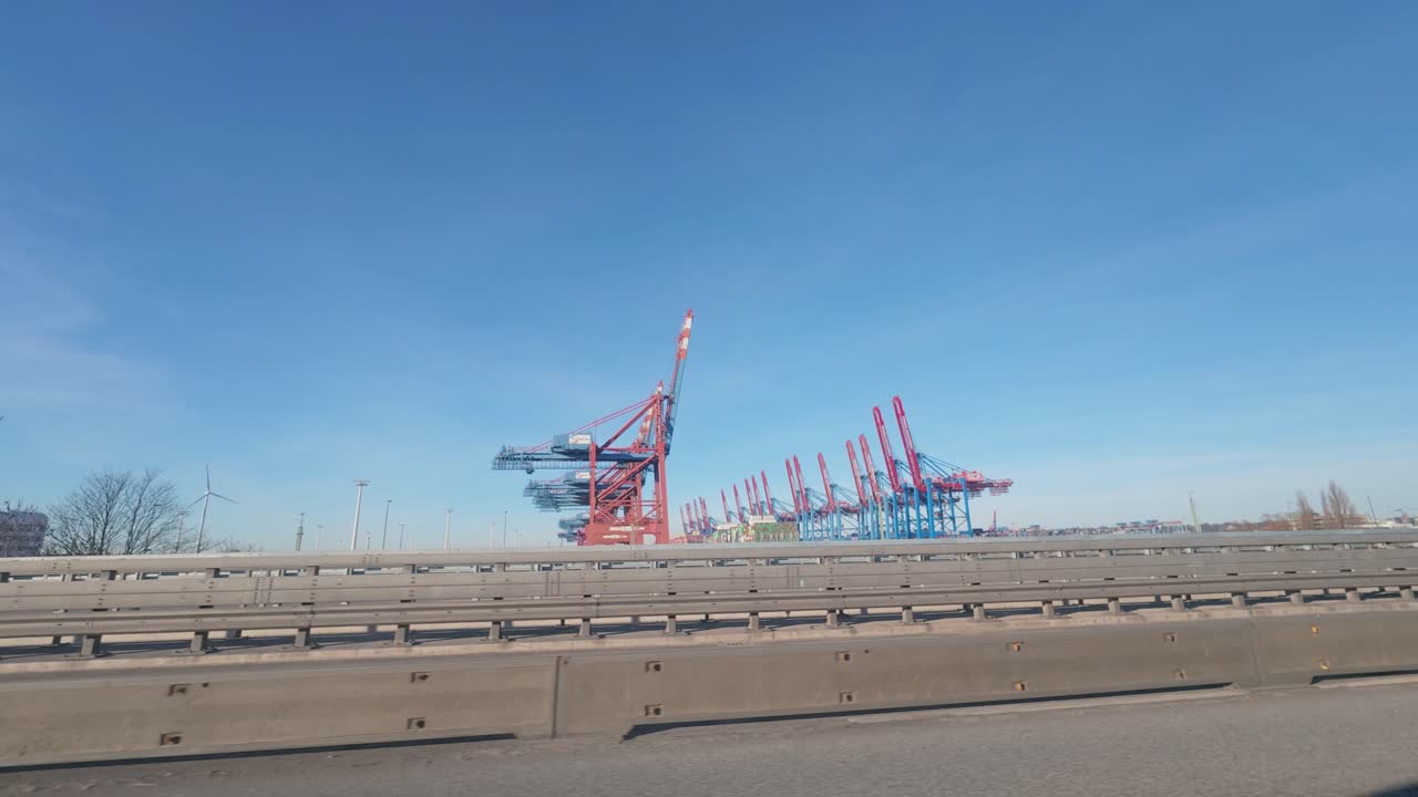 View from a moving car on the A7 highway toward Hamburg with container cranes at Waltershofer Hafen under blue sky
