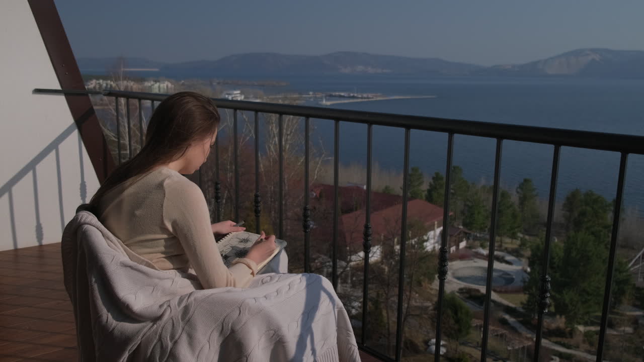 mujer dibujando en el balcón con vista al lago