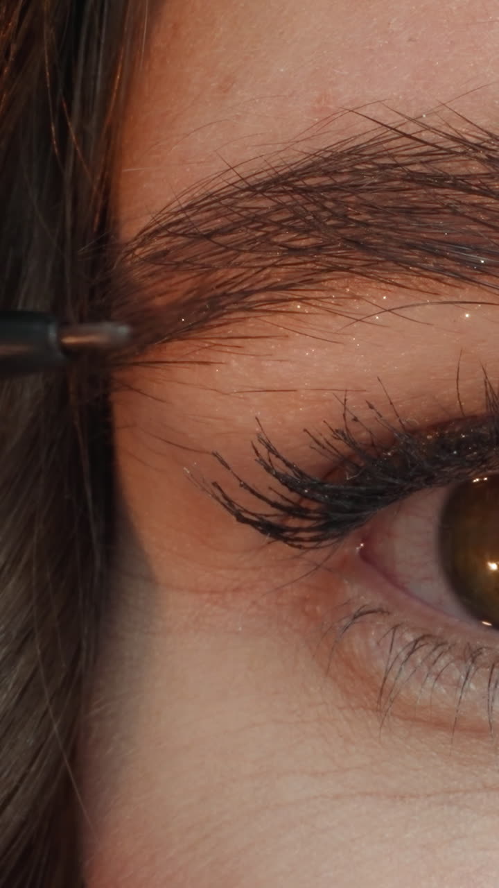 Young woman with brown eyes uses dark pencil to highlight contour of brows. Lady makes neat shape of eyebrows with cosmetic product macro