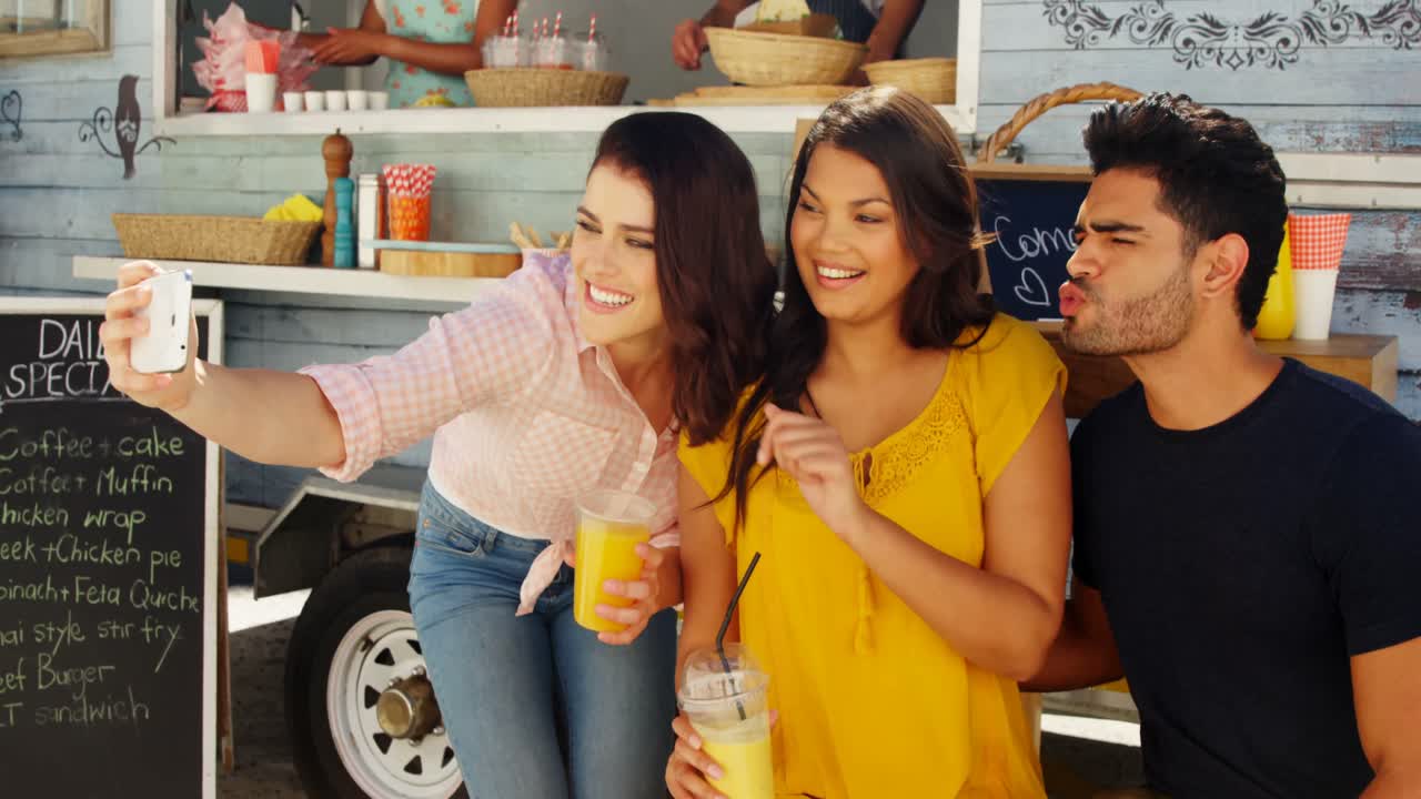 amigos tomando selfies desde teléfonos móviles en furgonetas de comida
