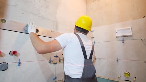 a builder in overalls is installing ceramic tiles in a bathroom repair in a new building