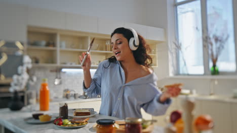 una mujer cantante preparando el desayuno con auriculares en la cocina de casa sola de cerca.
