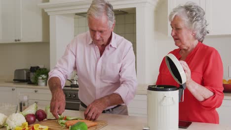 feliz pareja de ancianos caucásicos en la cocina preparando comida, compostando restos de verduras