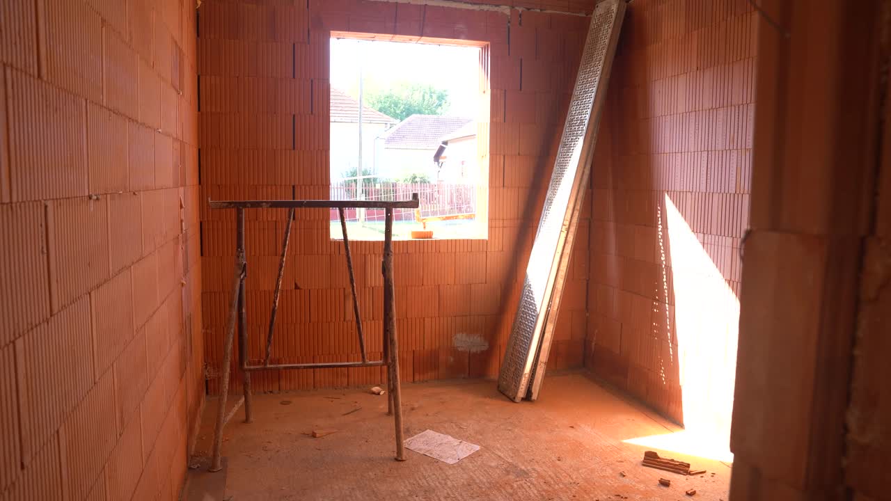 Sunlit unfinished room with window and scaffold at house construction site
