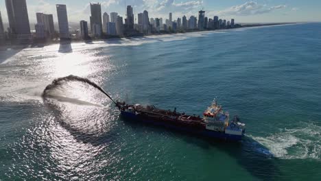 a dredging ship pumps sand to restore beach erosion along the gold coast, captured in bright daylight with city skyline
