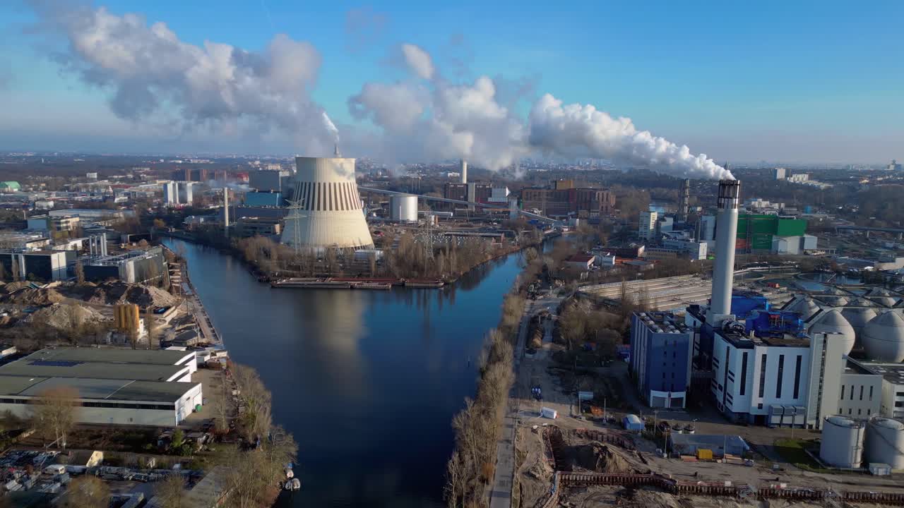 Aerial view of a thermal power plant emitting smoke on a sunny day, with a river and a city in the background. Lovely aerial view flight fly push forward drone
