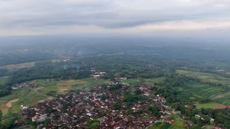 Misty-landscape-of-Indonesia-with-woodland-and-small-townships,-aerial-drone-view