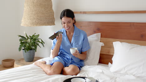 relaxing in bed, woman in pajamas enjoying coffee and talking on phone, at home