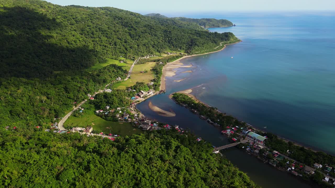 Seaside barangay town village with lush tropical greenery along turquoise lagoon and estuary at Batalay, Catanduanes, Philippines - aerial drone shot