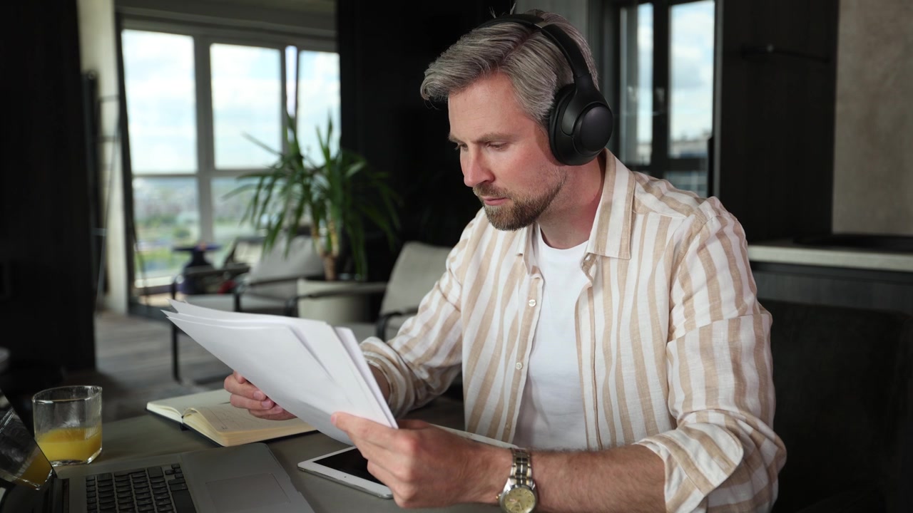 Man Wearing Headphones Reviewing Documents in Home Office