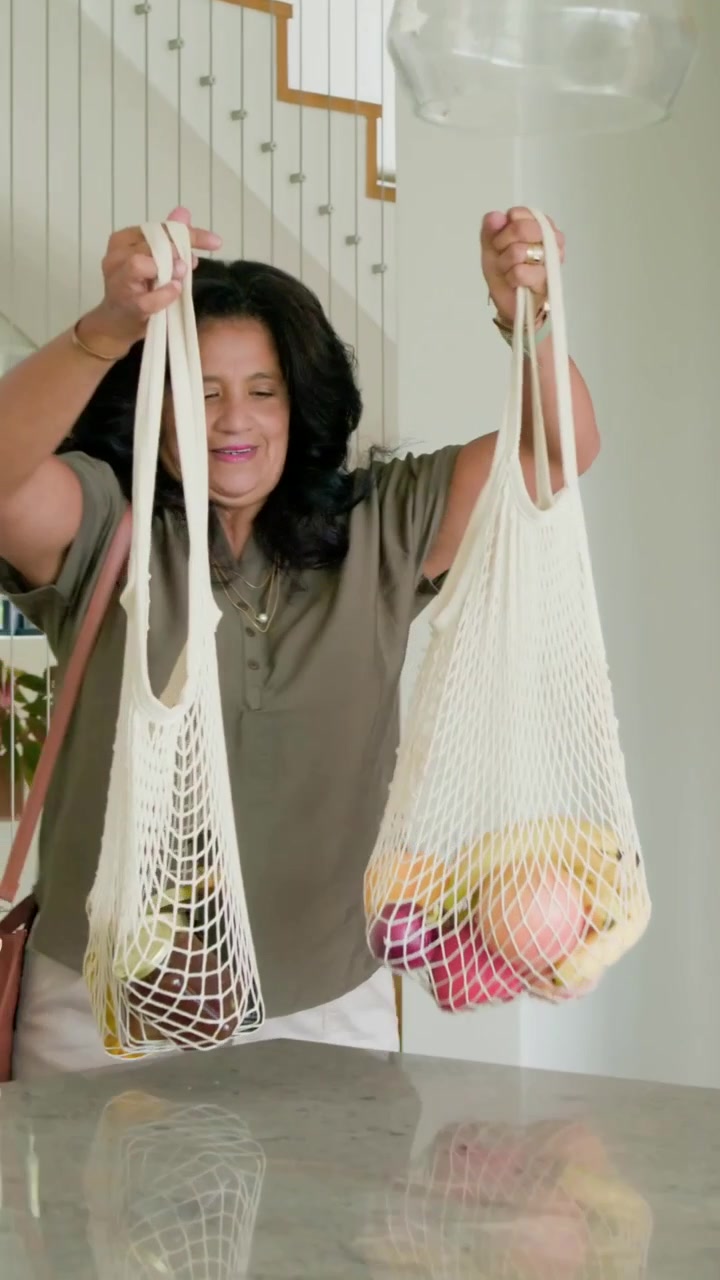 Video verticale: Donna entra portando borse a rete, disfa la spesa sull'isola della cucina e posa la borsa.