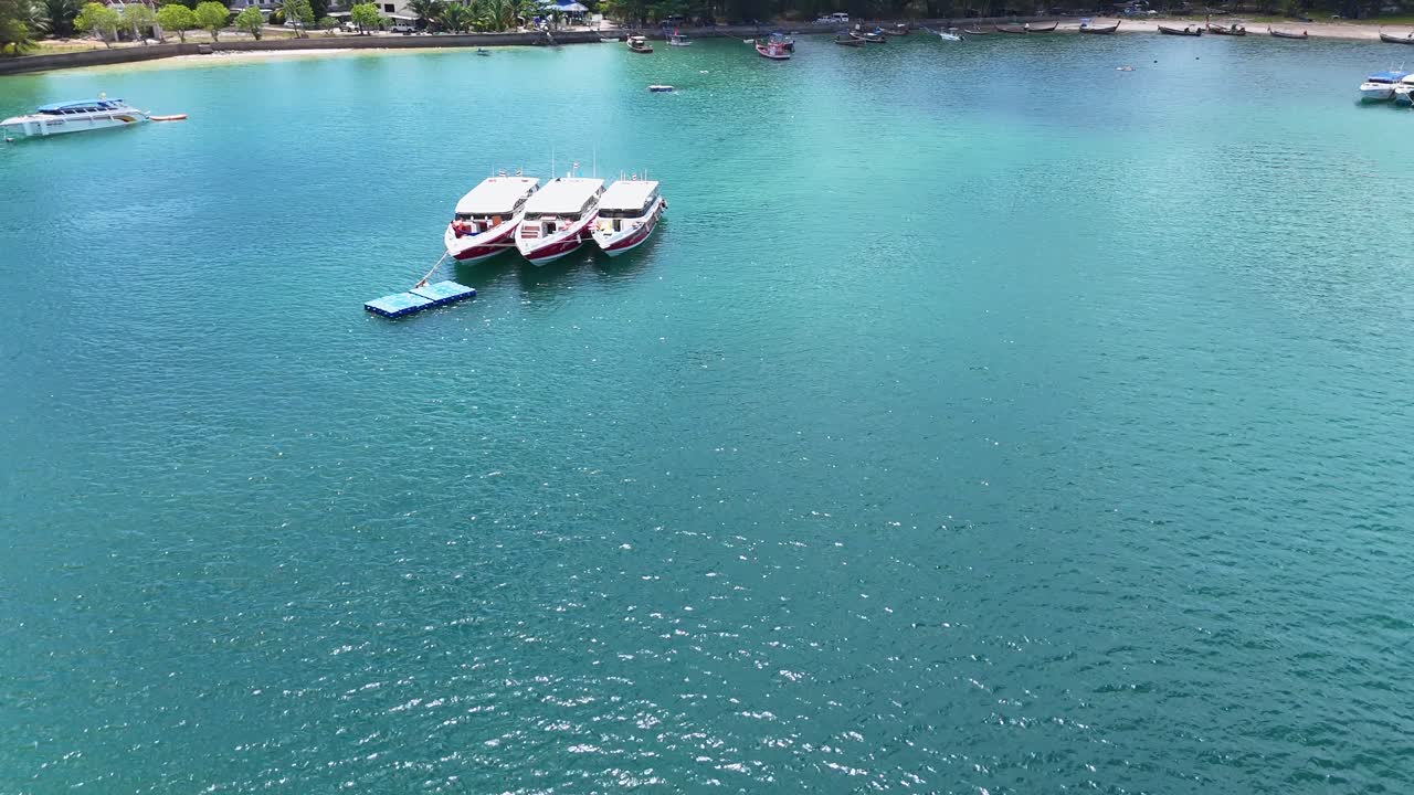 Drone footage captures boats on turquoise waters near a tropical beach in Phuket, Thailand, under bright daylight