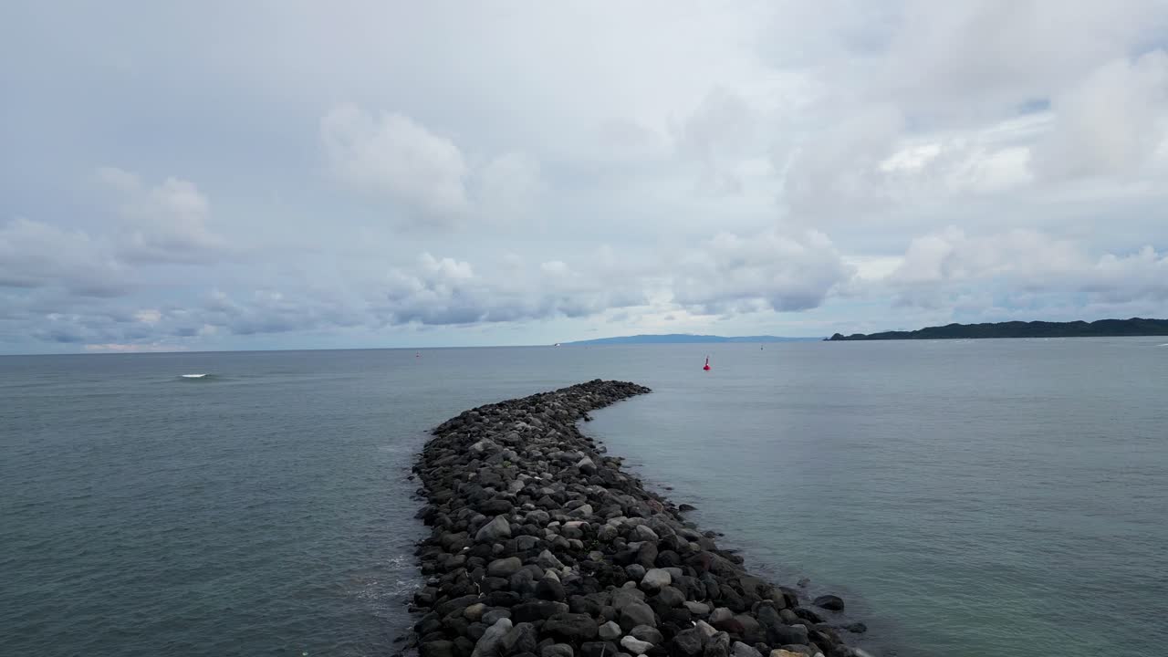 주황색 부표와 장엄한 클라우드스케이프가 배경에 있는 바위 방파제의 공중 드론 샷