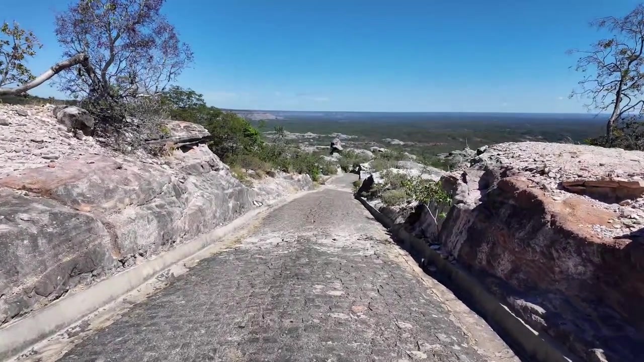 Una strada lastricata in pietra attraversa una scogliera rocciosa nel Parco Nazionale di Serra das Confusões, offrendo un'ampia vista panoramica sulla valle boscosa sottostante sotto un cielo limpido