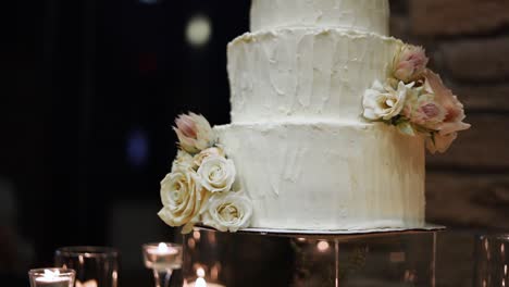 beautiful three-tiered wedding cake with minimal edible flower decoration, surrounded with candles on the table