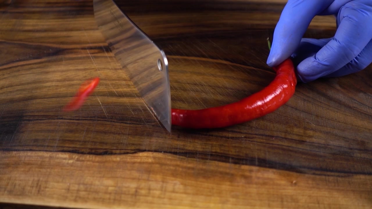 The cook cuts chilli pepper on a cutting board.