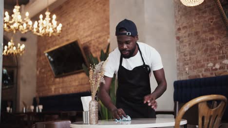 A-Black-person-in-a-black-apron-and-white-T-shirt-wipes-the-table-and-leaves-a-Reserved-sign.-High-quality-video