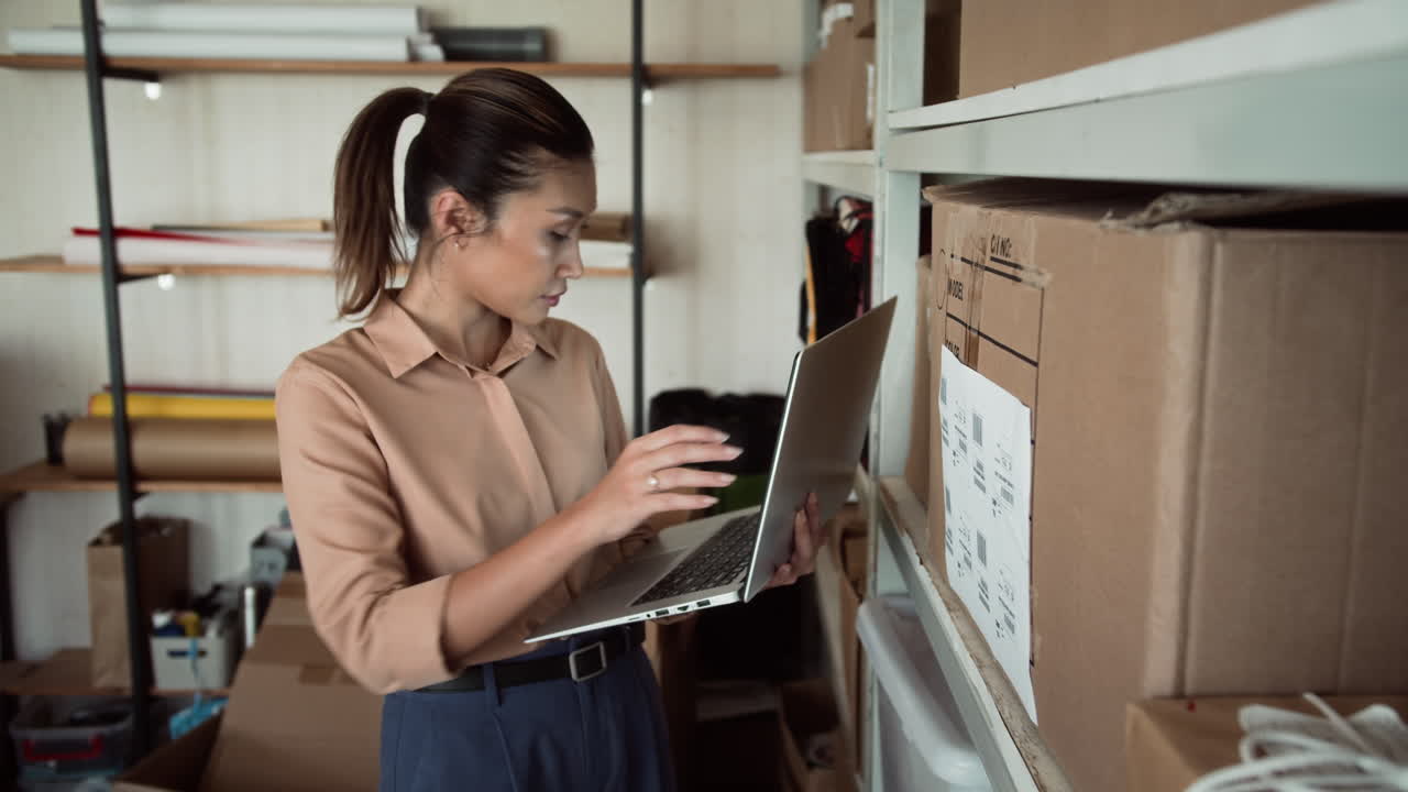 Delivery Service Woman Using Laptop while Searching for Parcels in Warehouse
