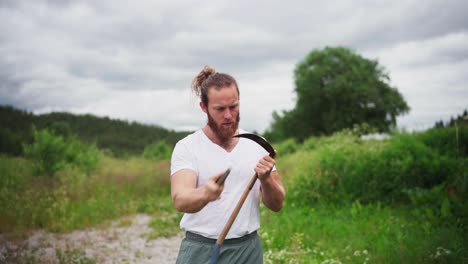 man sharpening blade of a scythe with sharpening stone outdoor