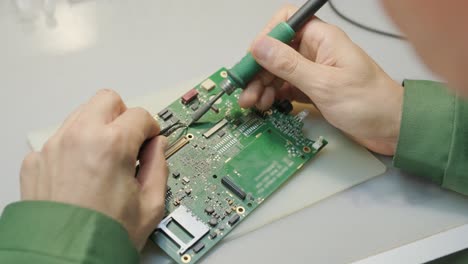 electronic equipment repair shop. the engineer technician solders the printed circuit board of an electronic device under a microscope.