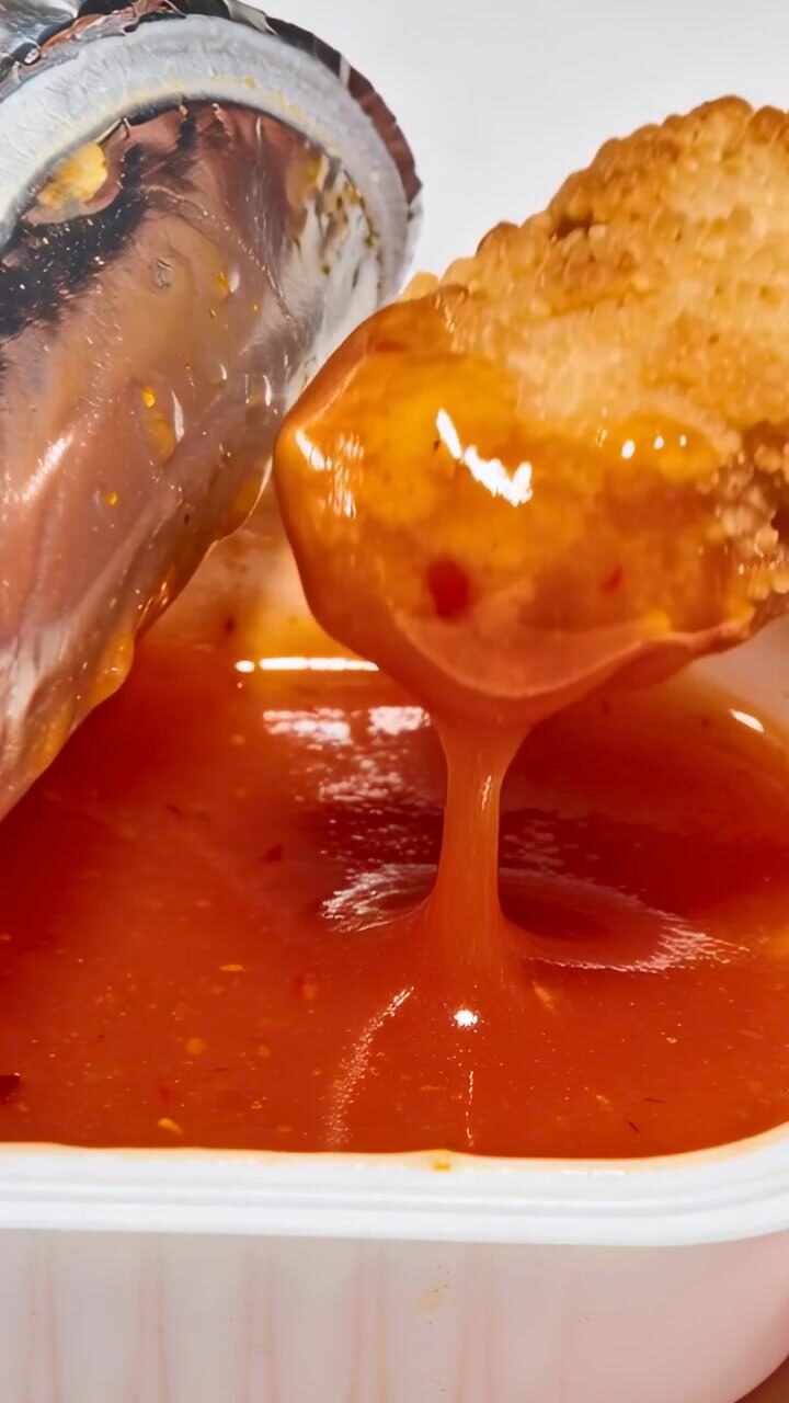 Video verticale: Mano che si allunga per intingere un nugget di pollo in una vaschetta di salsa bianca a tavola.