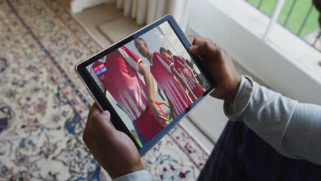 Composite-of-man-sitting-at-home,-watching-sports-event-on-tablet