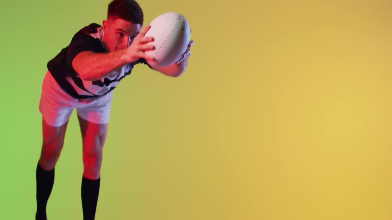 백인 남성 럭비 선수 가 노란색 조명 위 에 럭비 공 을 들고 점프 하고 있다