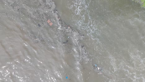 Top-down-aerial-drone-shot-over-polluted-sewage-water-and-floating-trash-with-debris-over-dead-coral-reef-mixing-with-turquoise-water-and-tropical-coastine-in-Bali-Indonesia